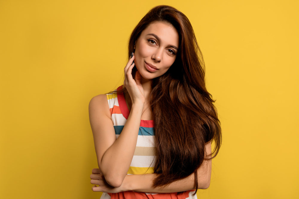 Una mujer con el cabello sedoso por utilizar acondicionador en un fondo amarillo