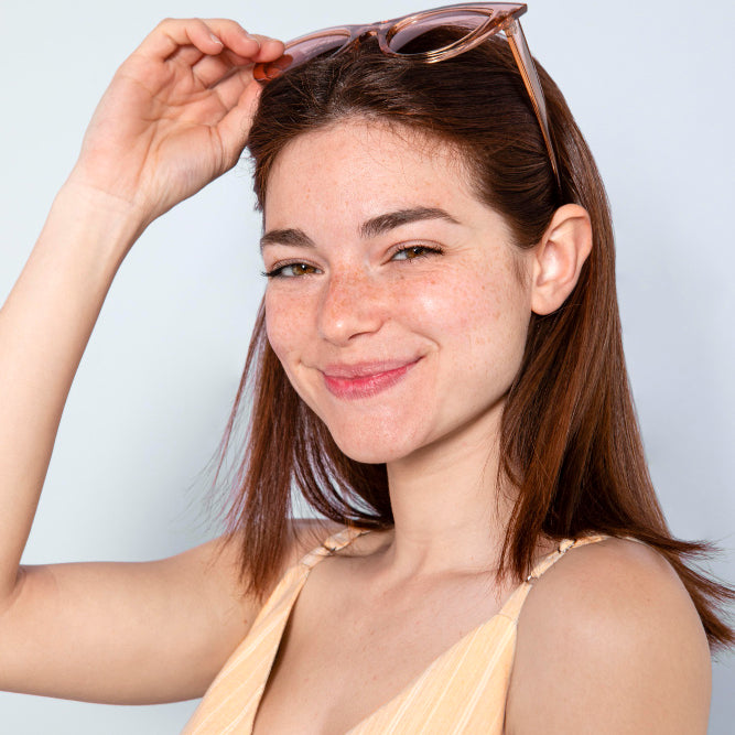 mujer joven con lentes de sol en su cabeza como diadema y top amarillo sonriendo por la frescura de su piel al usar tónicos