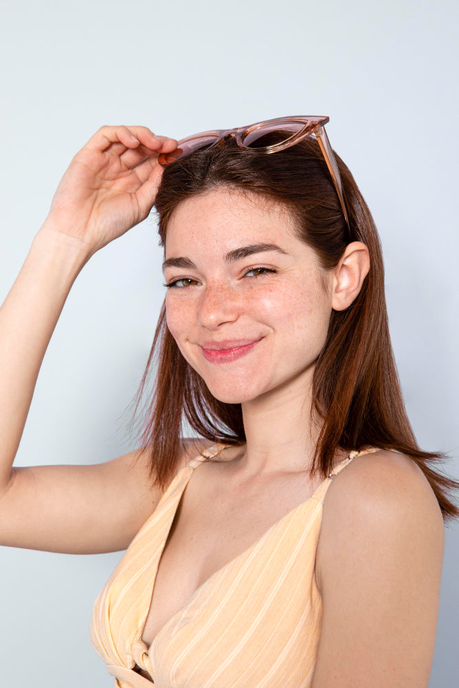 mujer joven con lentes de sol en su cabeza como diadema y top amarillo sonriendo por la frescura de su piel al usar tónicos