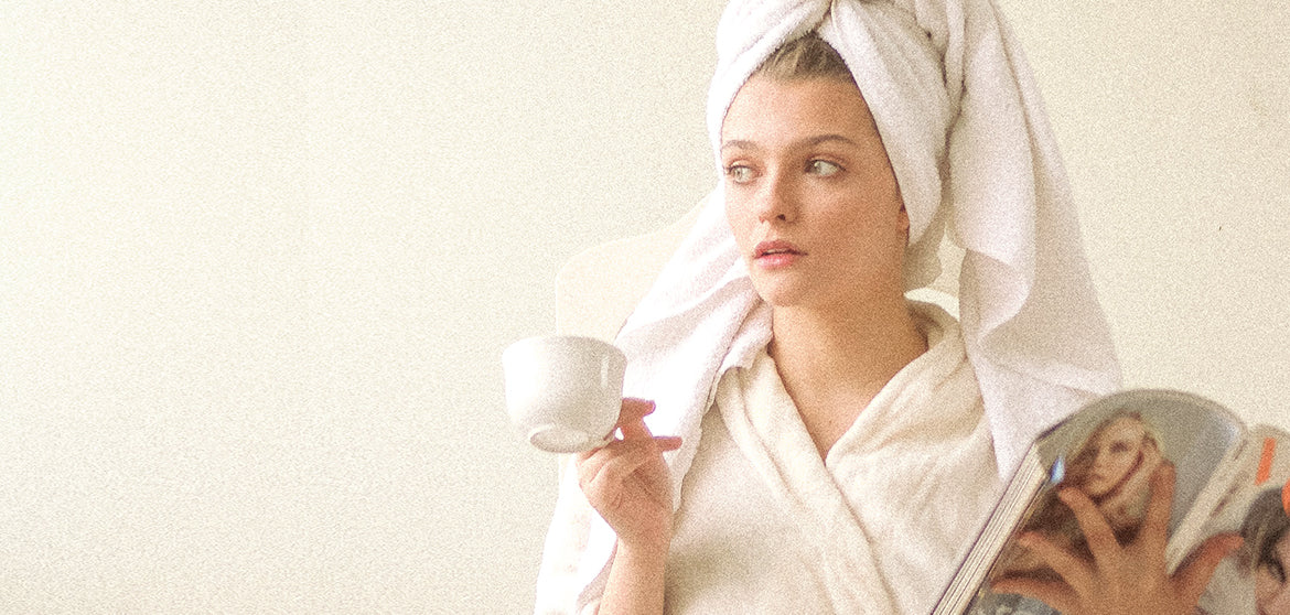 mujer después de un momento de cuidarse con su bata blanca, su toalla blanca, una revista de moda y un té de menta para el acné