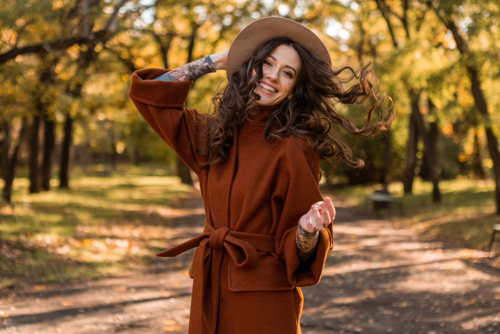 Uñas chocolate con una chica debajo de una arboleda en otoño mostrando un outfit que combina con los tonos de la temporada