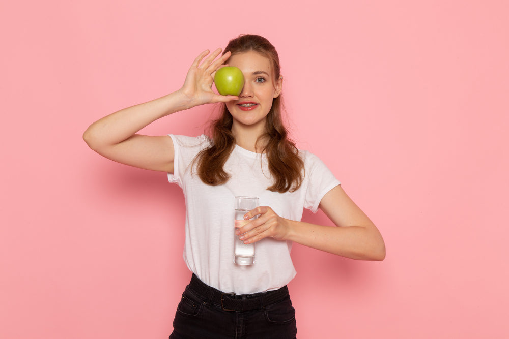 joven mujer sosteniendo una manzana y agua para indicar las vitamina naturales o en suplementos que dan una piel deslumbrante