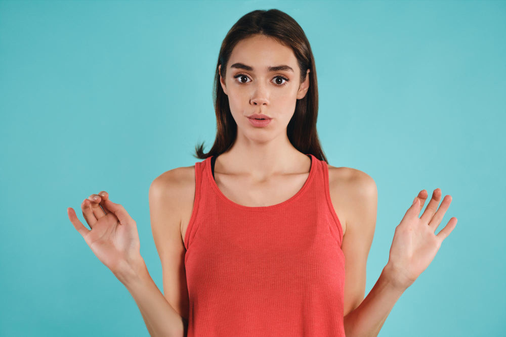 chica joven haciendo yoga facial con una blusa anaranjada y un fondo azul pastel